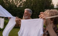 Elderly man and teenage boy working together, hanging laundry in a green outdoor setting.
